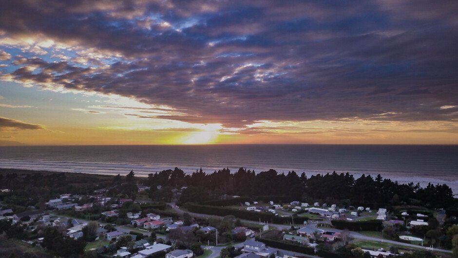 Sunset over the Leithfield settlement and its belt of pine, the long open sweep of Pegasus Bay running north to the horizon, 