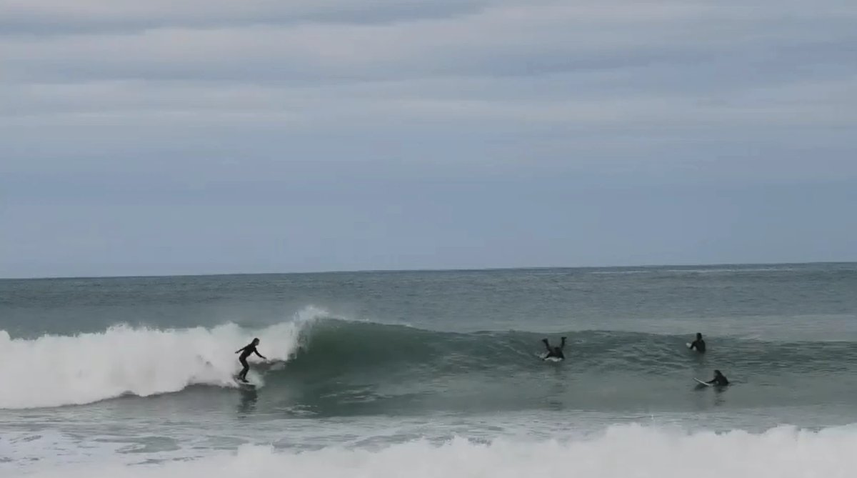 A froth of locals trading the lefts on a grey, glassy Banks Peninsula day, Magnet Bay surf spot, Canterbury, New Zealand.