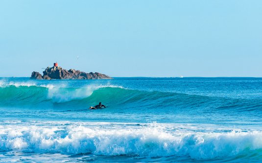 Surfer paddling out near the Moturiki rock formations, Mt Maunganui - Main Beach surf spot, Bay of Plenty, New Zealand.