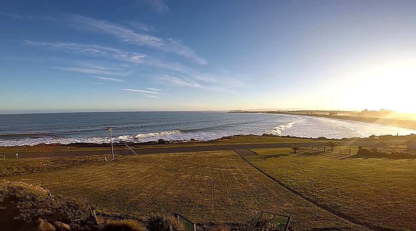 Low winter sun over the bay at Oamaru, swell lines marching into an empty beach below the paddocks, Oamaru surf spot, Dunedin