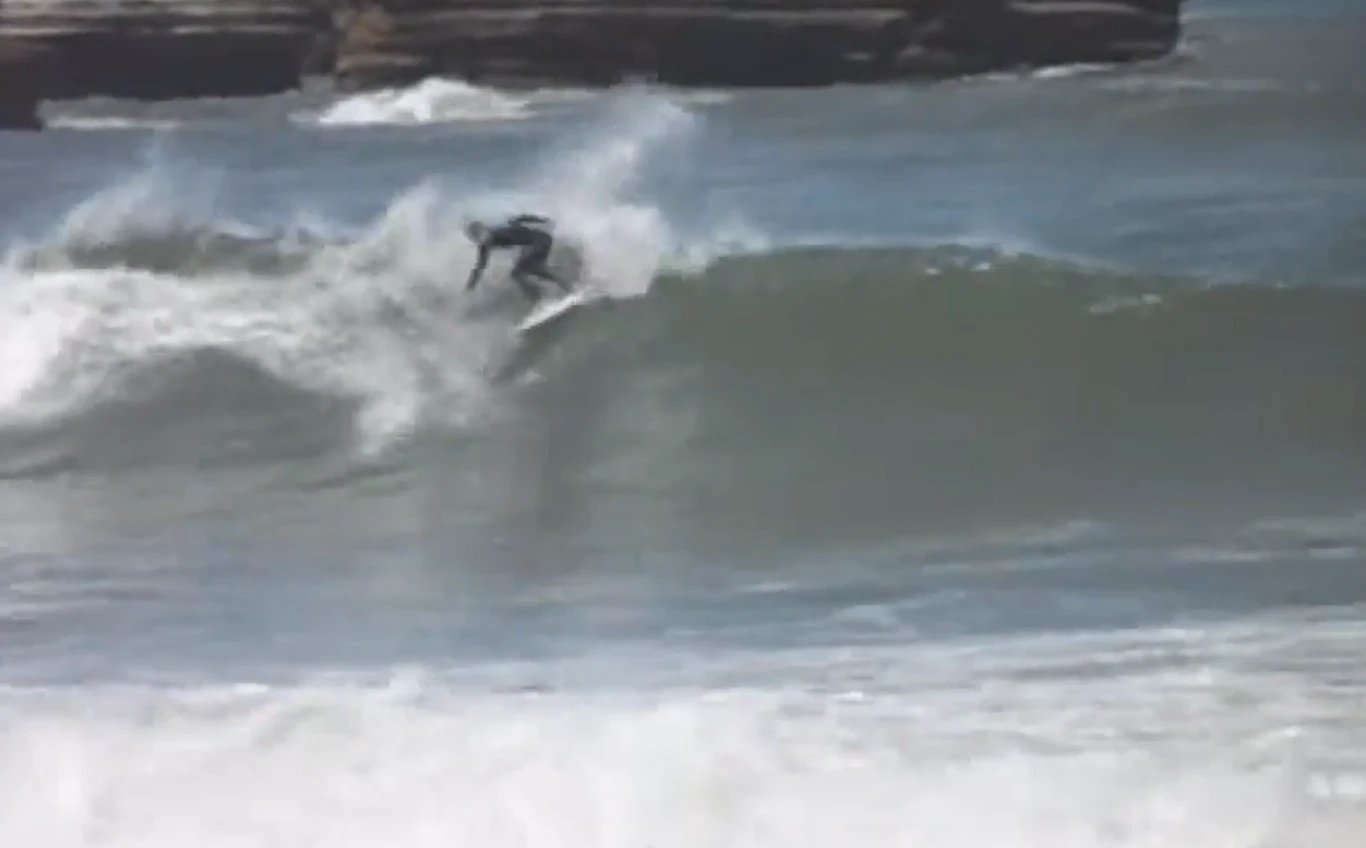 A surfer drives off the bottom on a solid Punakaiki wall, dark cliffs framing the lineup, Punakaiki surf spot, West Coast Sou