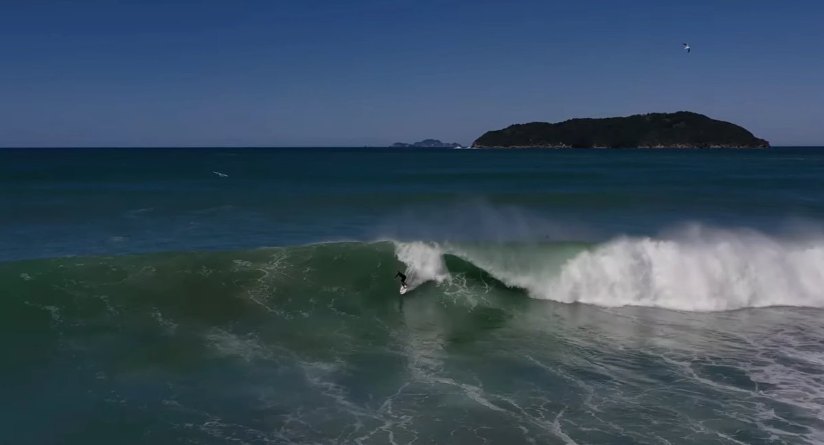 Big-day drone shot with the headland and offshore islands behind, Tairua surf spot, Coromandel, New Zealand.