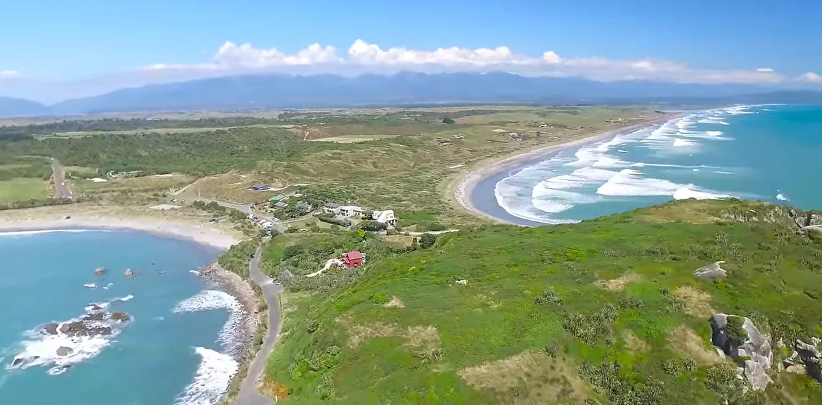 The wider sweep of the bay from above, beach houses, the seal colony headland and the ranges away inland, Tauranga Bay surf s