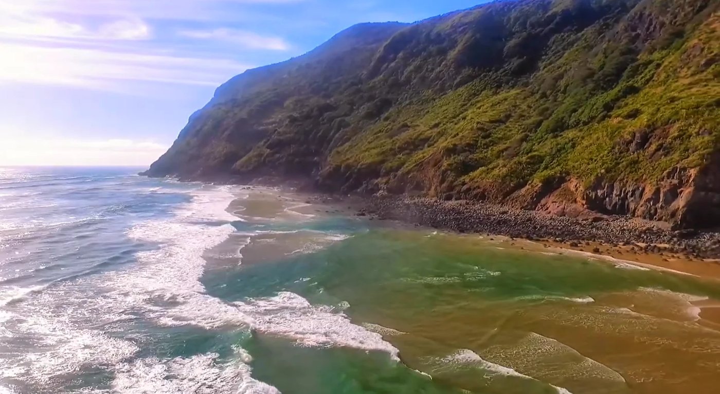 Green water meeting sand at the foot of the cliffs, The Bluff surf spot, Northland West, New Zealand.