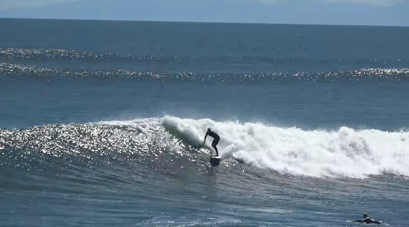 A surfer drops into a glassy West Coast wall in the morning sun off the Buller River mouth, Westport surf spot, West Coast So
